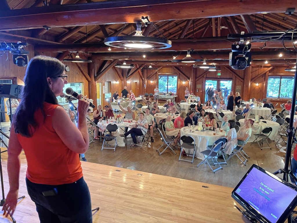 Guest singing karaoke on stage in front of a large seated crowd at a private party